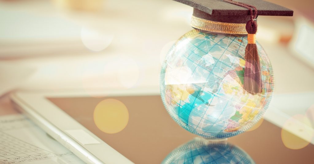A light-colored digital globe with a graduation cap and tassel on top of its surface sits on a display screen.