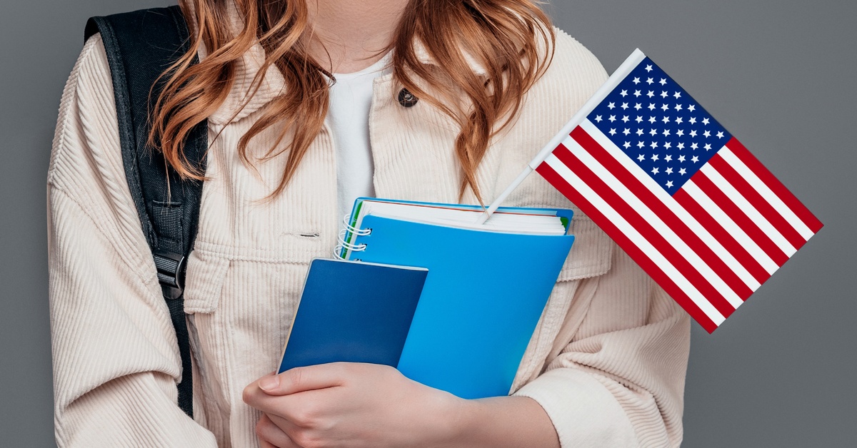 A person with long hair holding two blue books of different sizes, one of which has an American flag inside it.