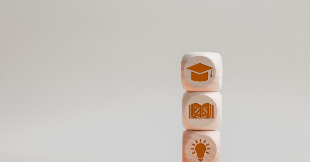 Three blocks stacked together, one with a light bulb icon, one with a textbook icon, and one with a graduation cap icon.