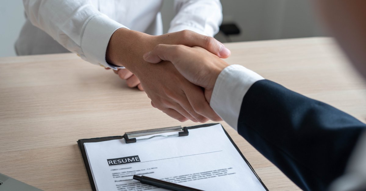 The arms of two people sitting across from each other at a table, extended toward one another as they shake hands.