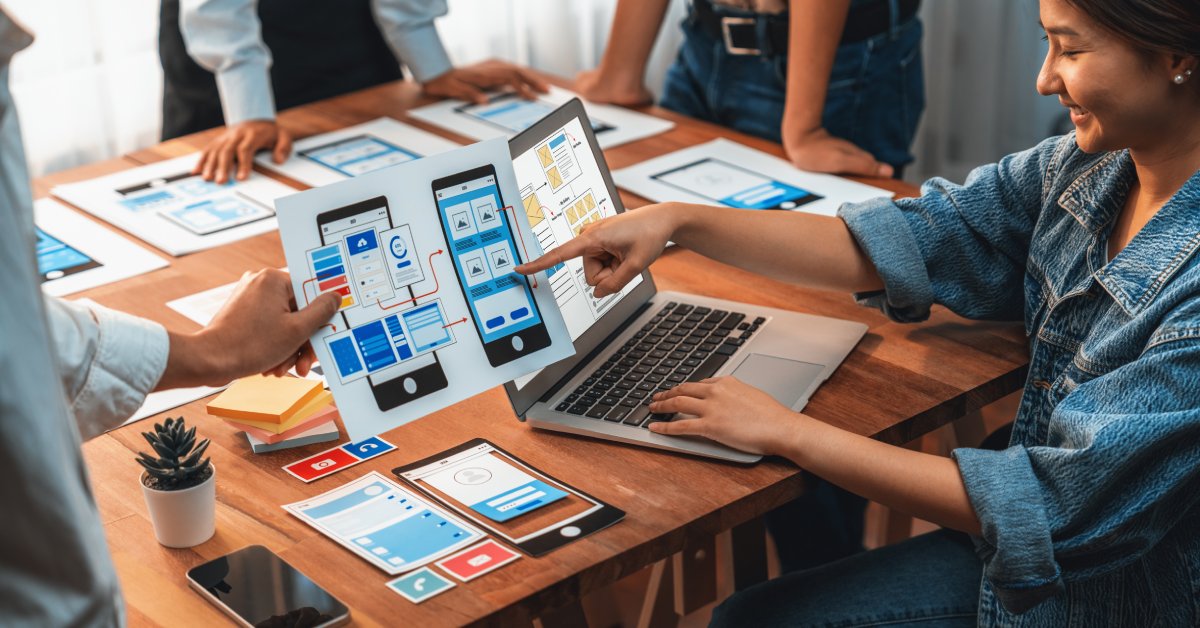 A group of students or coworkers is collaborating on a web mobile app development project at a table.