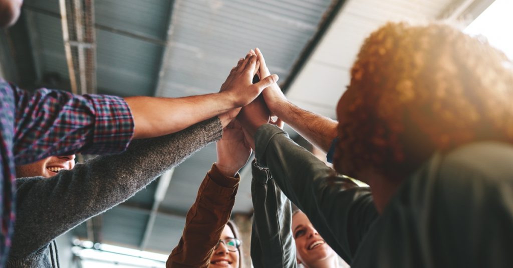 A group of diverse people gives each other one big high-five to celebrate something in a professional setting.