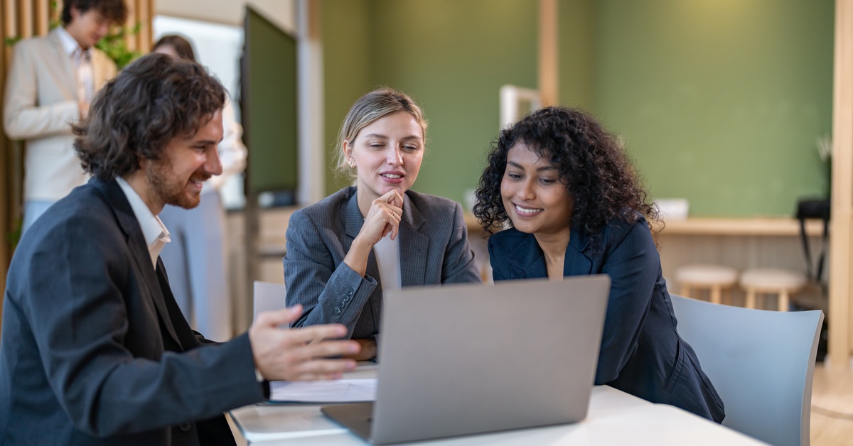 A diverse tech team of two women and one man is meeting in a coffee shop to discuss a software project on a laptop.