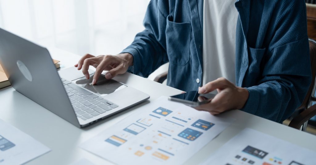 A close-up of a UX/UI Designer working on innovative mobile app ideas using paper wireframes at their workspace.