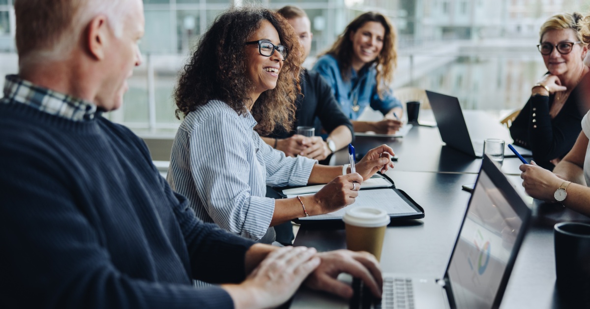 A close-up of a group of diverse business people having a meeting in a boardroom. A woman with curly hair is speaking.