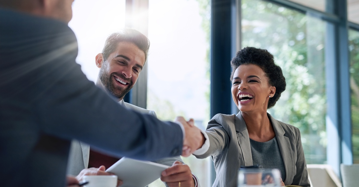 Three diverse businesspeople smile and shake hands in the office for a deal, collaboration, or onboarding.