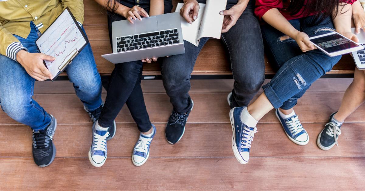 A group of students and their shoes and sneakers as they use their laptops outside on a college campus.