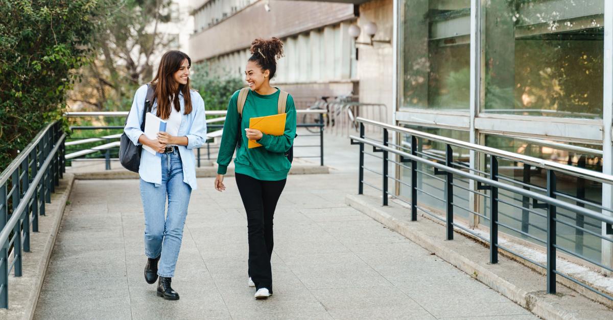 Two happy students, young women, walking and talking to each other on the university campus after classes.
