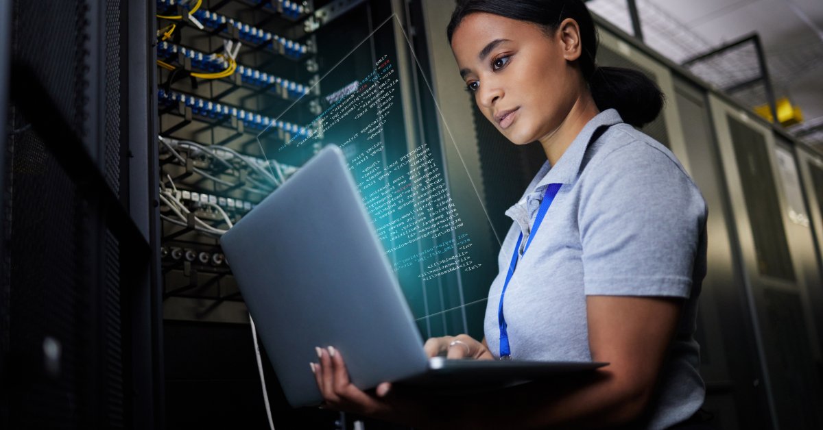 Technician uses a laptop beside server racks and network cables, with a digital code overlay across the equipment.